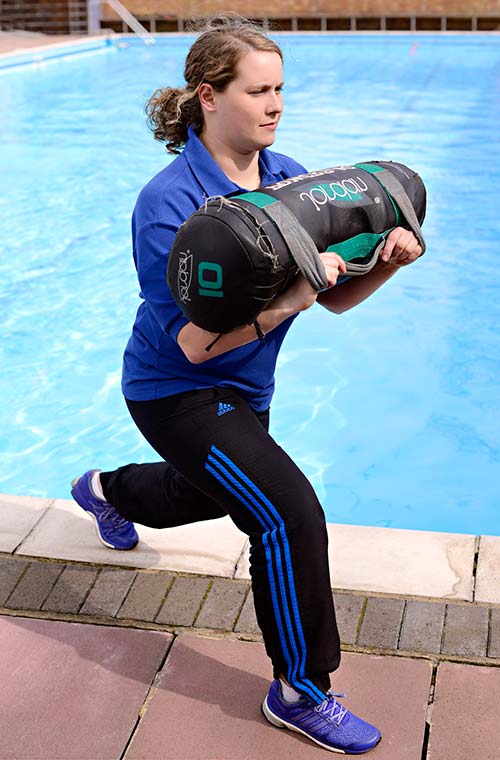 Bex lifting a punchbag weight next to a swimming pool