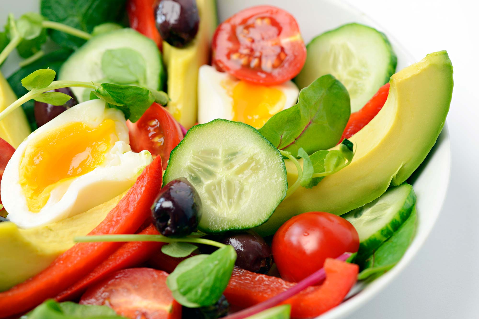 A bowl of fruit, fresh vegetables, leaves and half a poached egg